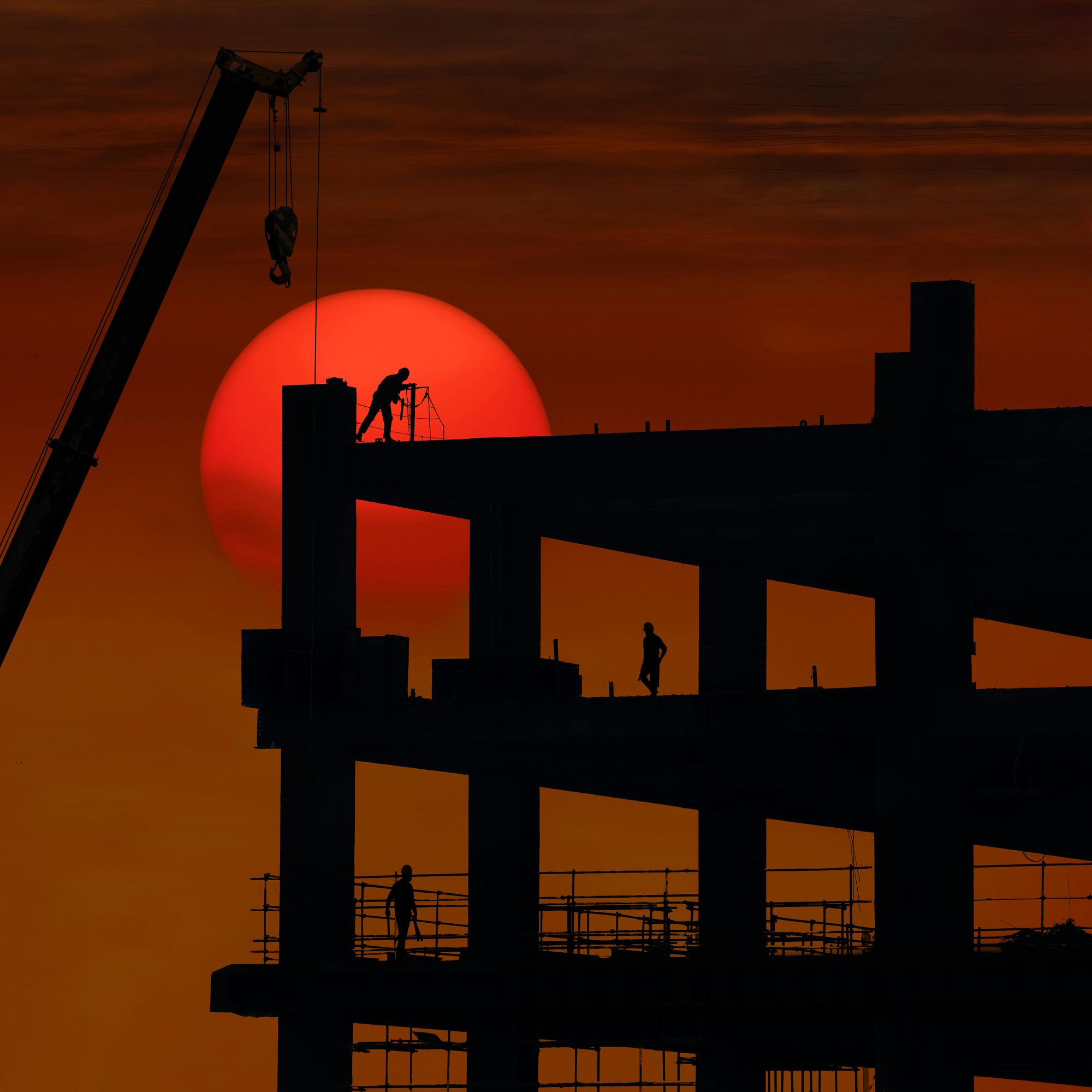Construction workers silhouetted on a steel frame against a red sunset